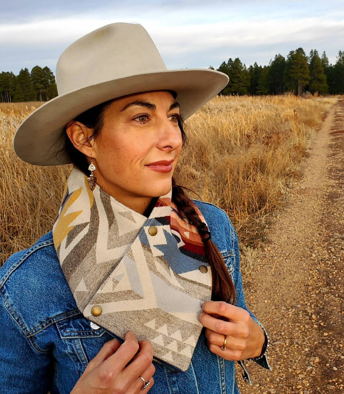 Western cowl neck scarf is worn by model in wetland area. Wild Rag looks similar to bandana or neck gaiter. Made with Pendleton® wool, the design features pink, yellow, tan, blue geometric shapes that are popular in the Southwest.