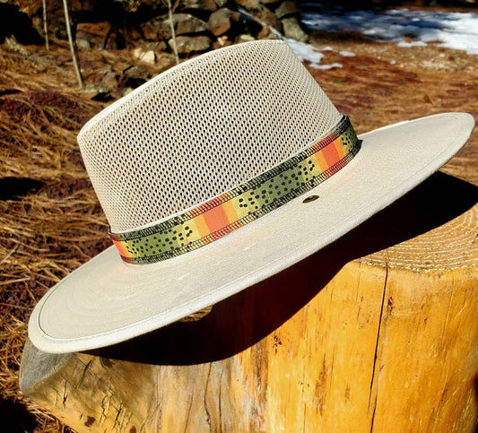 Light beige river hat leaning on wooden stump, featuring cutthroat trout patterned hat band. Hat band has yellow, green, orange coloring with black speckles mimicking the coloring of cutthroat trout.