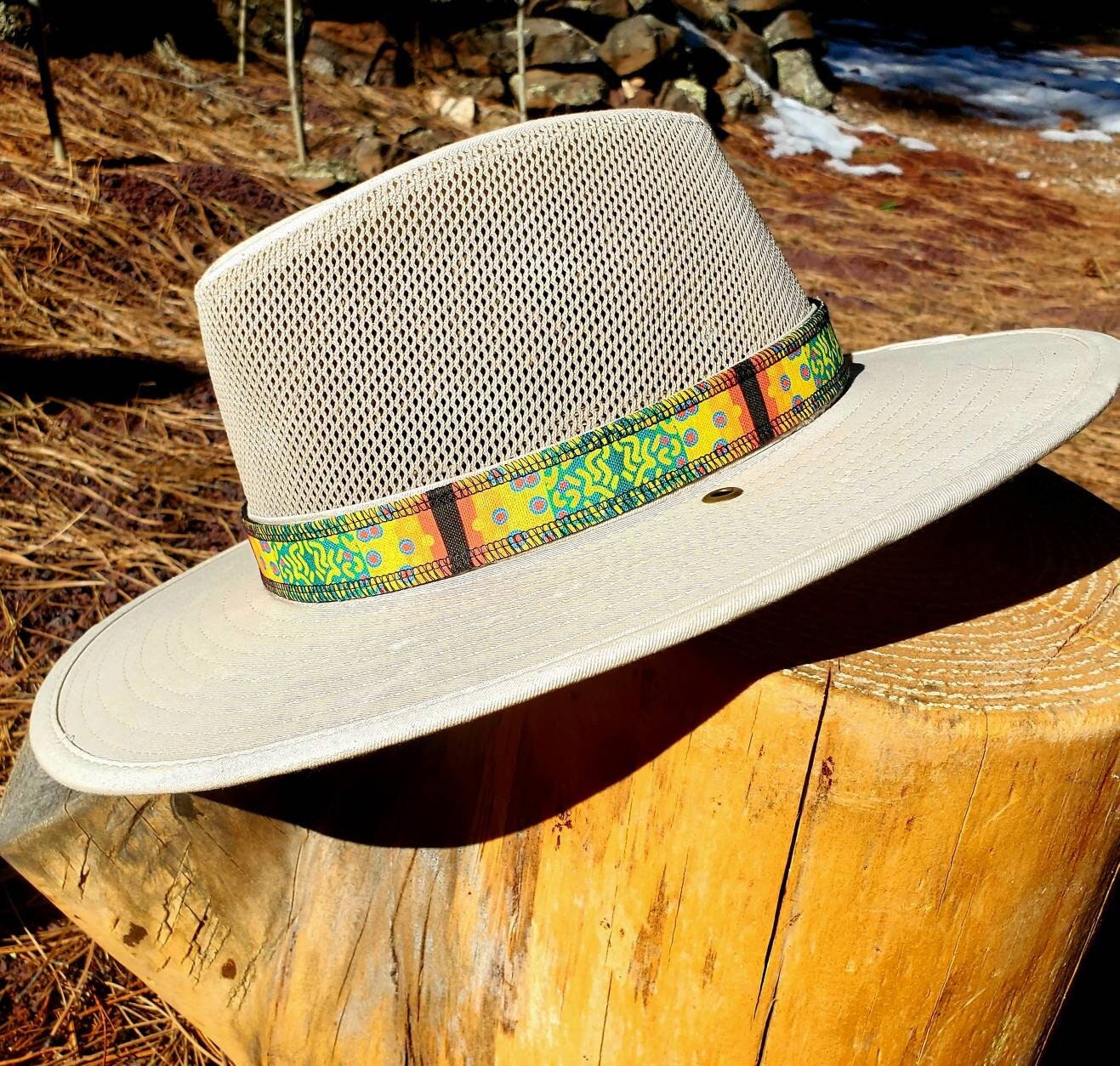 Light beige river hat leaning on wooden stump, featuring brook trout patterned hat band. Hat band has yellow, green, orange coloring with speckles mimicking the coloring of brook trout.