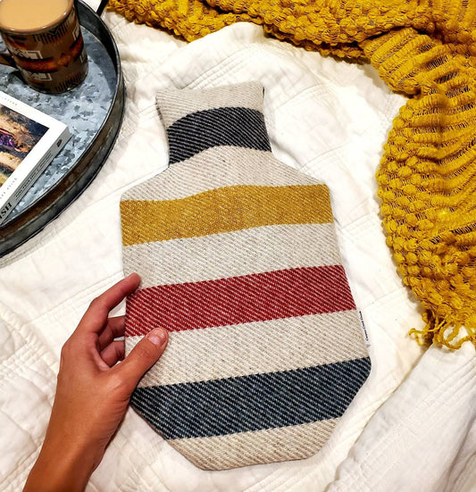 Hot water bottle laying on bed, made with Pendleton® wool and features iconic Glacier National Park fabric.