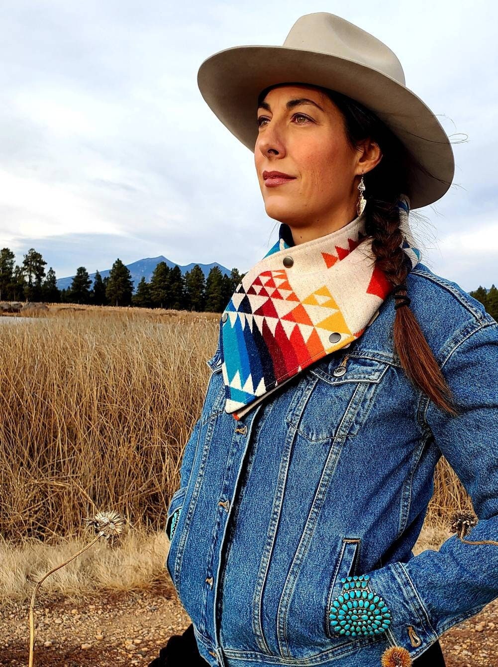 Western cowl neck scarf is worn by model standing in wetlands. Scarf looks similar to bandana or neck gaiter. Made with Pendleton® blanket-weight wool, the design features rainbow colored geometric shapes that are popular in the Southwest.