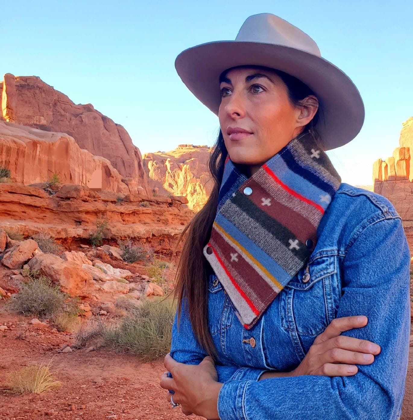 Western cowl neck scarf is displayed on model overlooking red rocks. Made with Pendleton® blanket-weight wool, the design features blue, brown, tan, red geometric shapes that are popular in the Southwest.