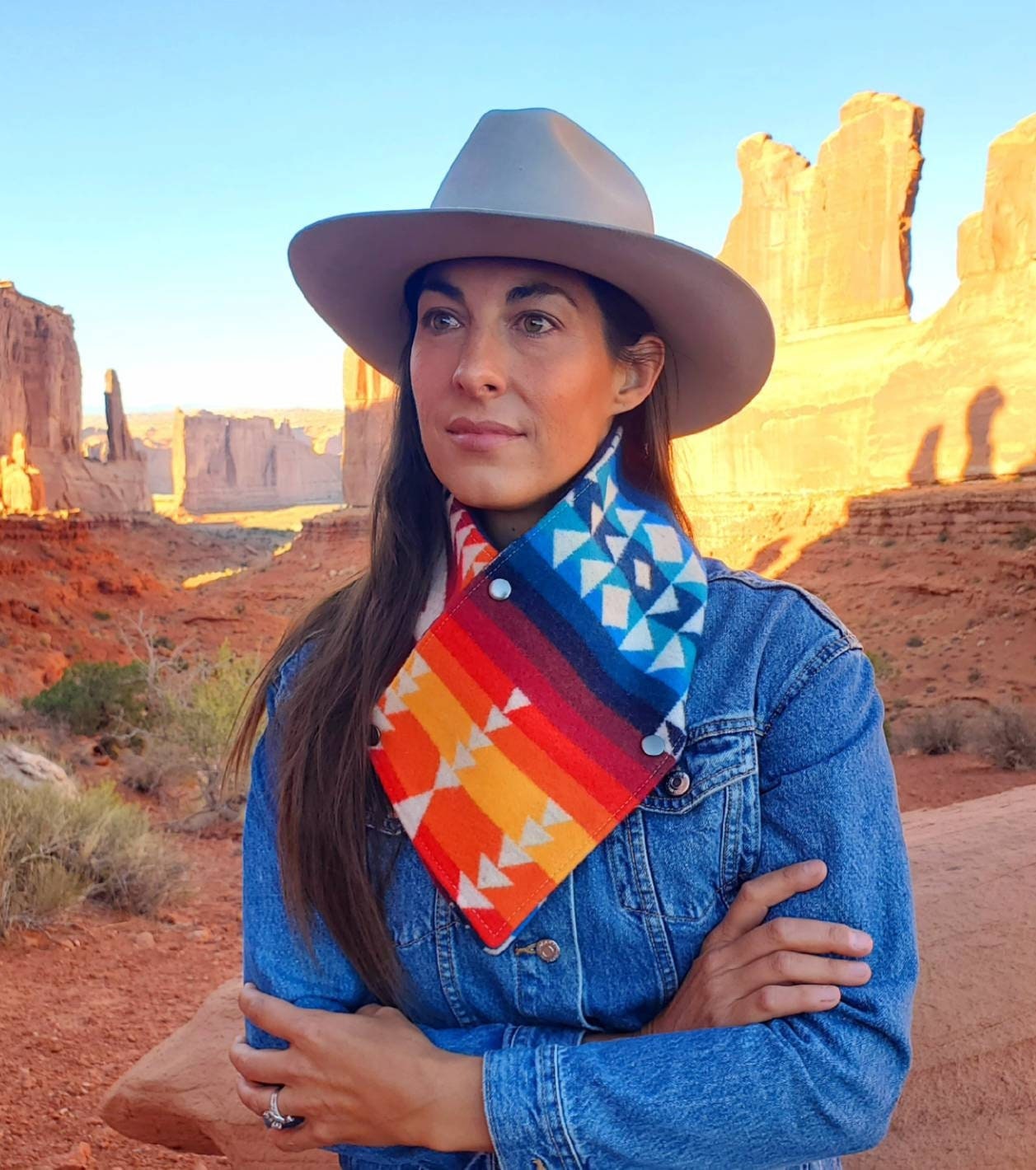 Western cowl neck scarf is worn by model overlooking red rocks. Scarf looks similar to bandana or neck gaiter. Made with Pendleton® blanket-weight wool, the design features rainbow colored geometric shapes that are popular in the Southwest.