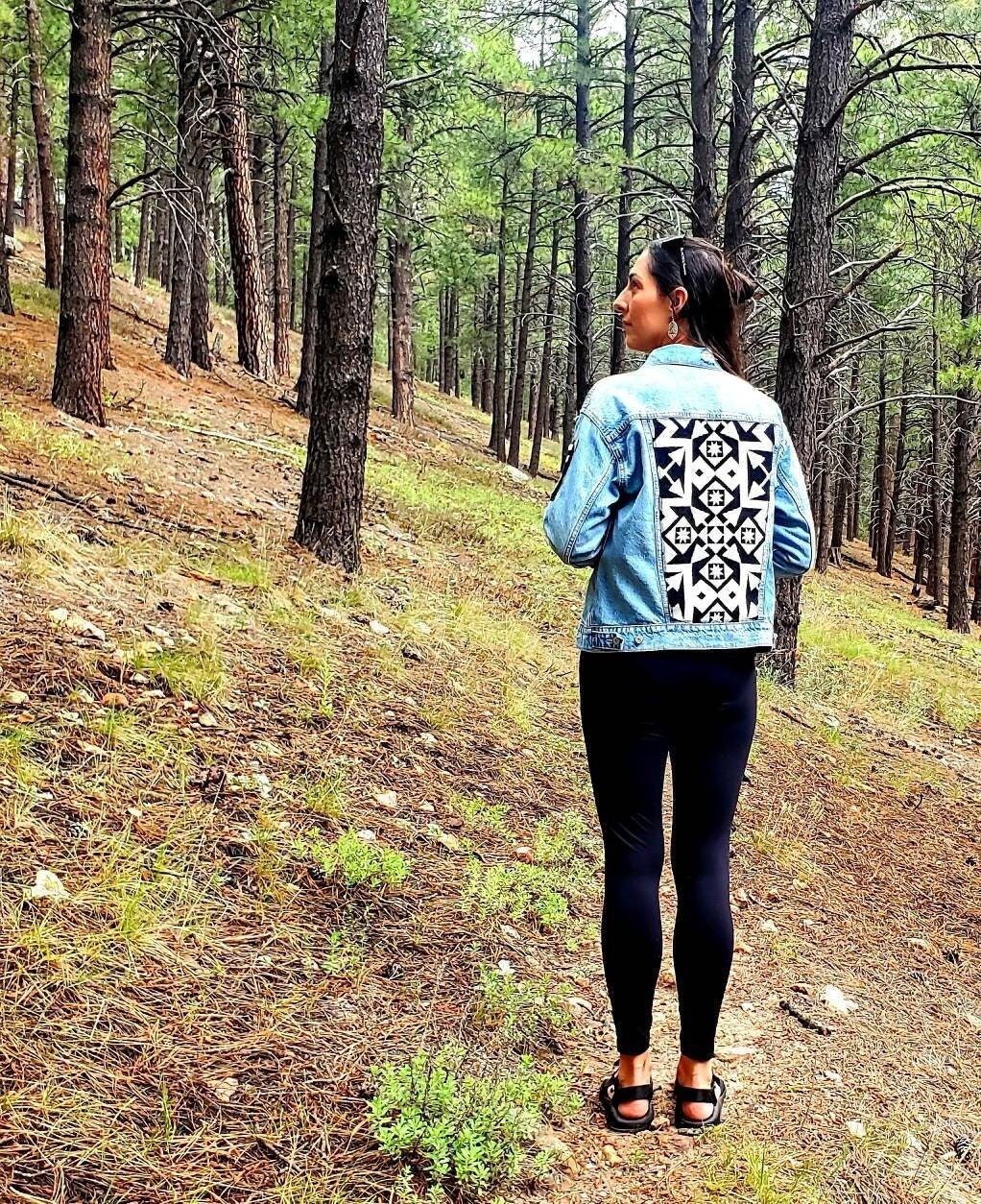 Model standing in forest wearing upcycled denim jacket with black and white Pendleton® wool patches.