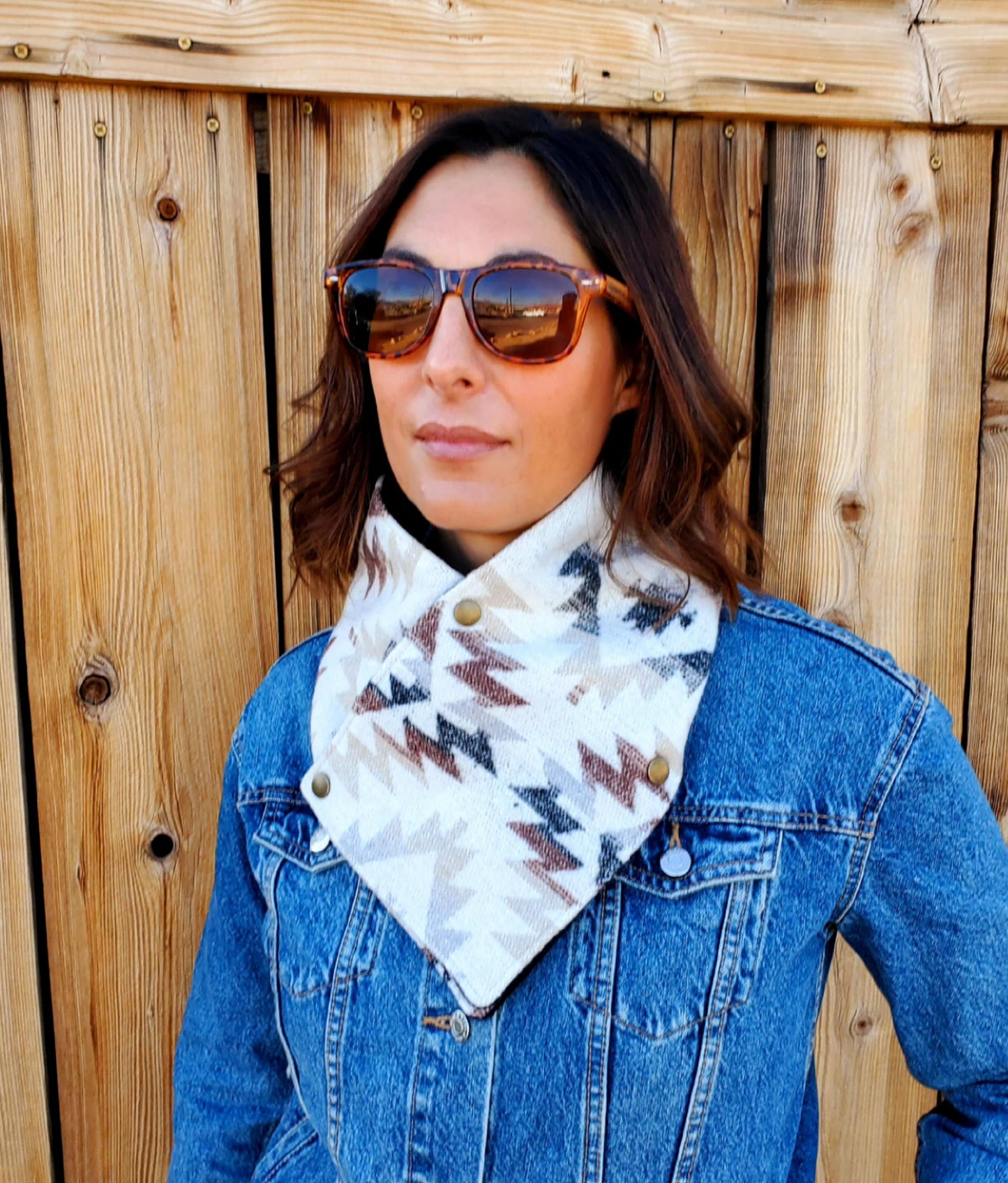 Model wearing western cowl, neck scarf made of wool and lined with fleece. Scarf is white with brown, black and grey geometric designs.