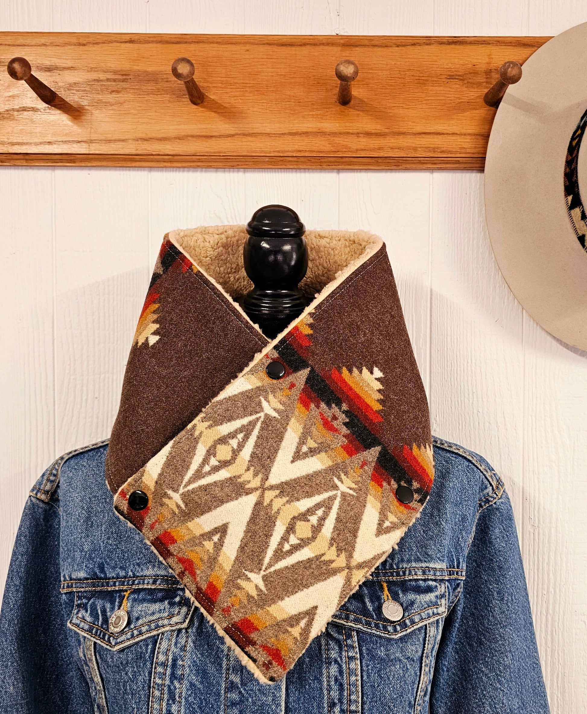 Western cowl neck scarf is displayed on mannequin & looks similar to bandana or neck gaiter. Made with Pendleton® blanket-weight wool, the design features black, brown, tan and white geometric shapes that are popular in the Southwest.